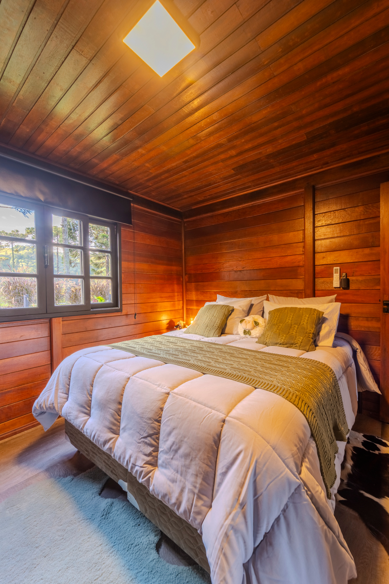 Quarto em madeira com cama queen, vista para araucárias